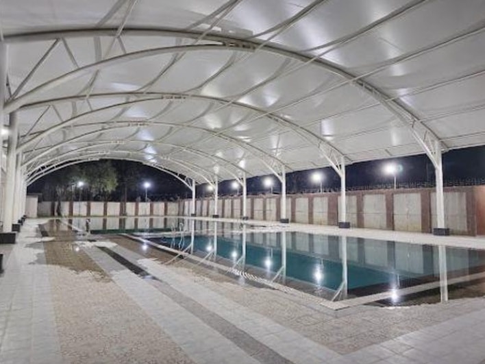 Clear-span illuminated arched tensile membrane roof over swimming pool