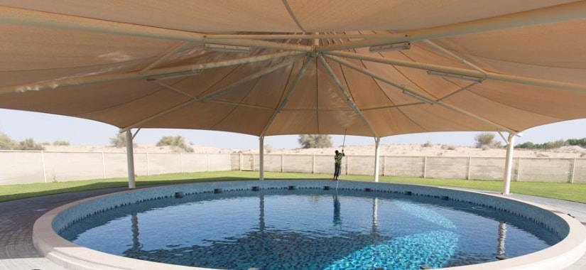 Conical umbrella tensile shade structure over circular swimming pool